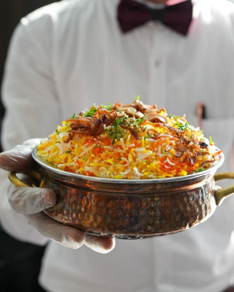 Waiter serving copper handi of Kewat's Dum Biryani